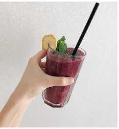 Hand holding Glass with maroon coloured juice and a black straw in it