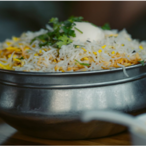 Biryani in a stainless steel bowl garnished with coriander