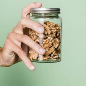 Hand holding a closed glass jar of walnuts